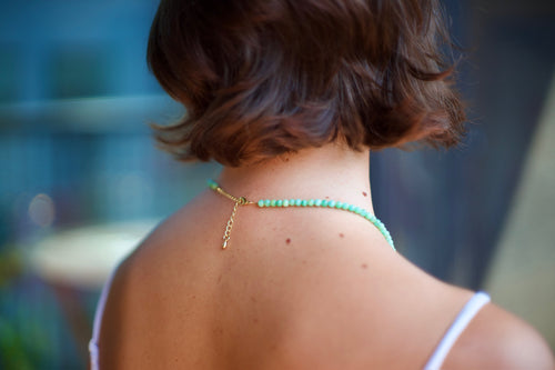 A close-up back view of a woman with short brown hair wearing a delicate mint green beaded necklace with a gold clasp and chain.