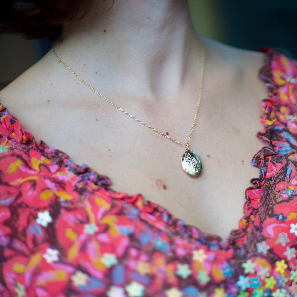 A close-up shot of a person wearing a delicate gold chain necklace with a small oval pendant, paired with a vibrant pink and red floral-patterned top.