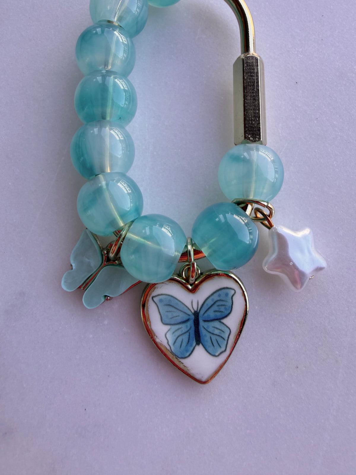 A gold bag charm features blue beads with a white star, blue butterfly heart charm, and a blue butterfly. close up of charms