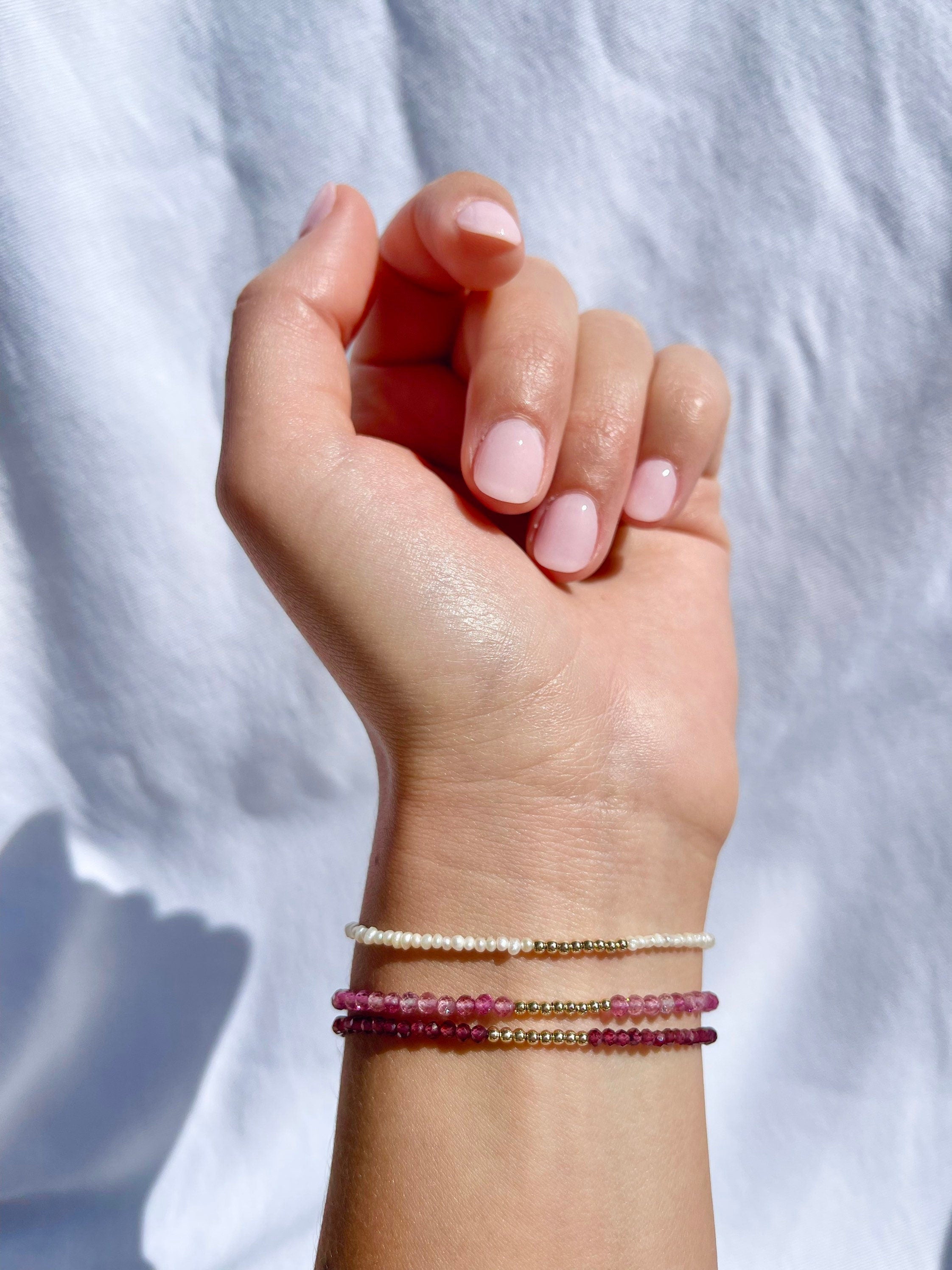 handmade birthstone bracelet stack styled on wrist featuring garnet, pink tourmaline and pearl stones 